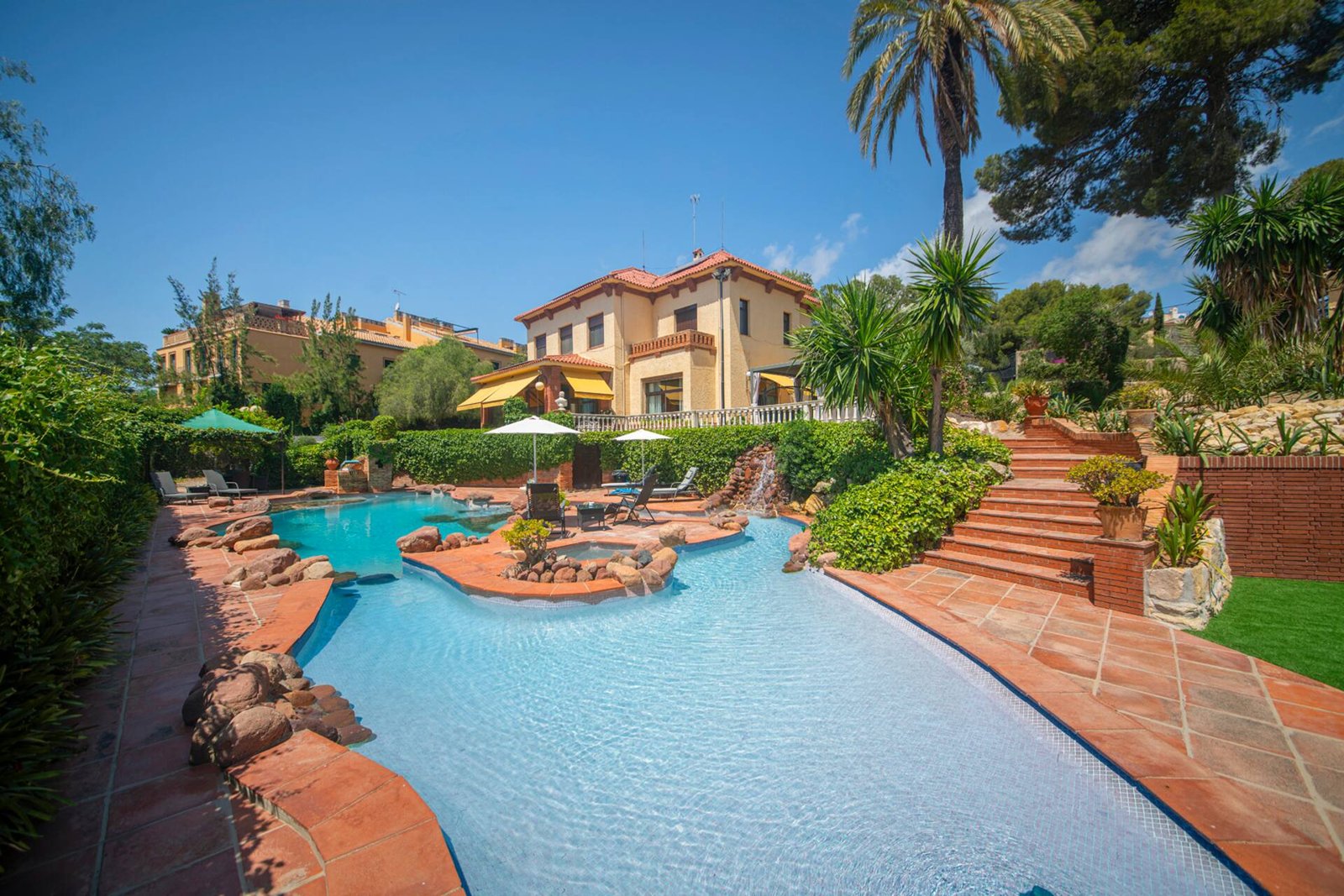La villa vista desde la piscina de roca, con la palmera y el cielo azul